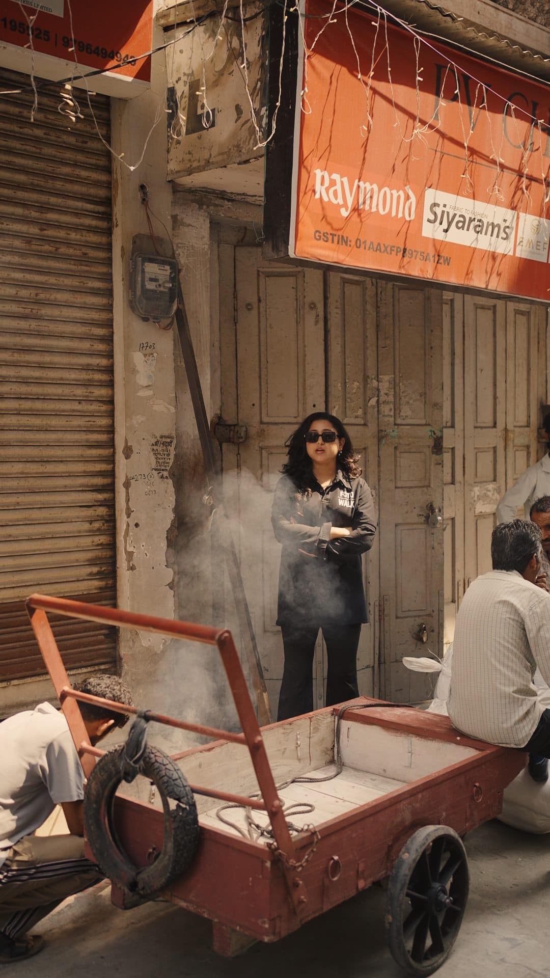 A crew member standing in a smoky street beside a hand cart