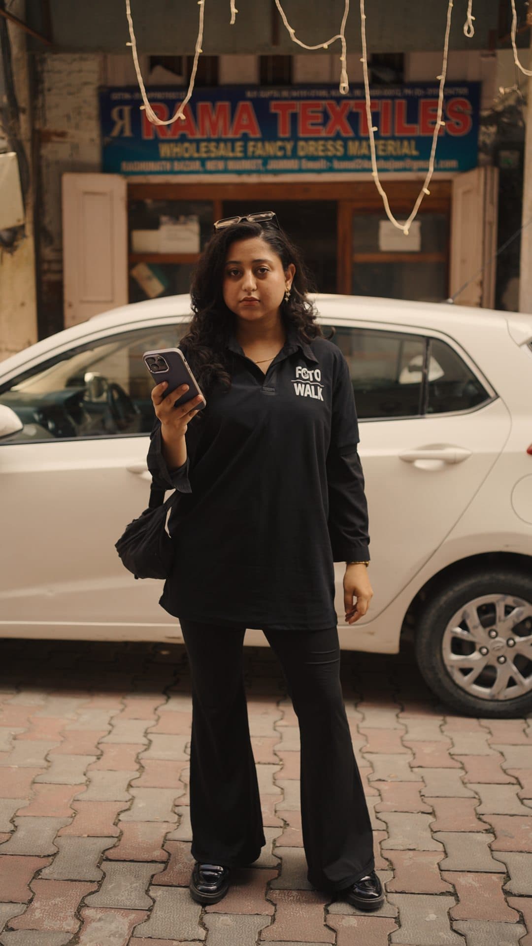 A crew member checking her phone beside a parked white car