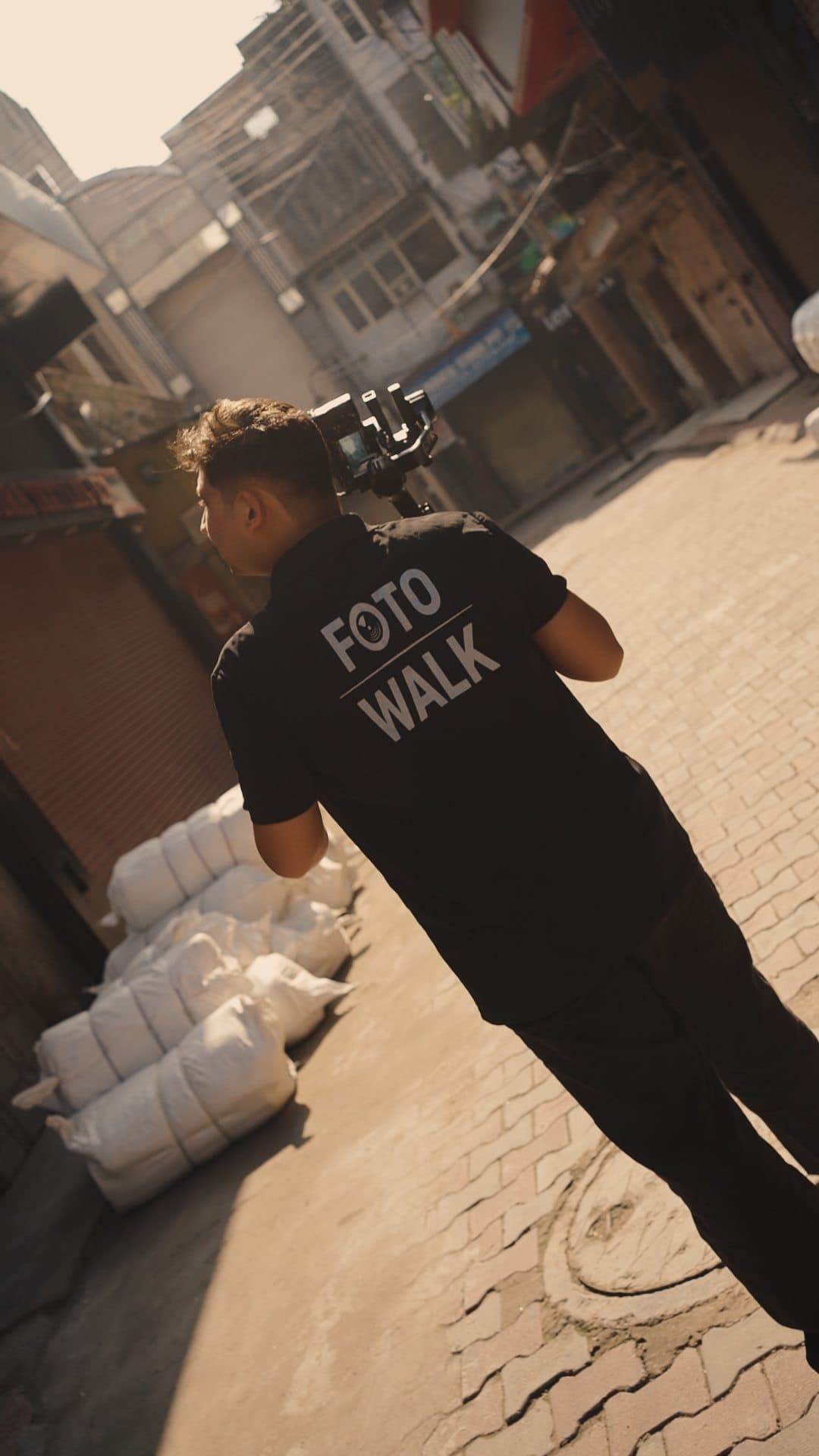 Crew member walking away down an alley, FotoWalk printed on the back of his shirt